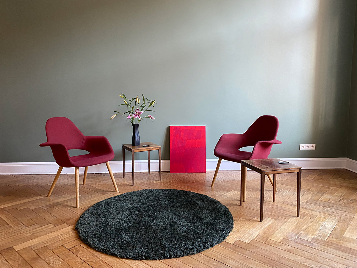 Der eingerichtete Praxisraum mit zwei roten Sesseln und einem roten Teppich